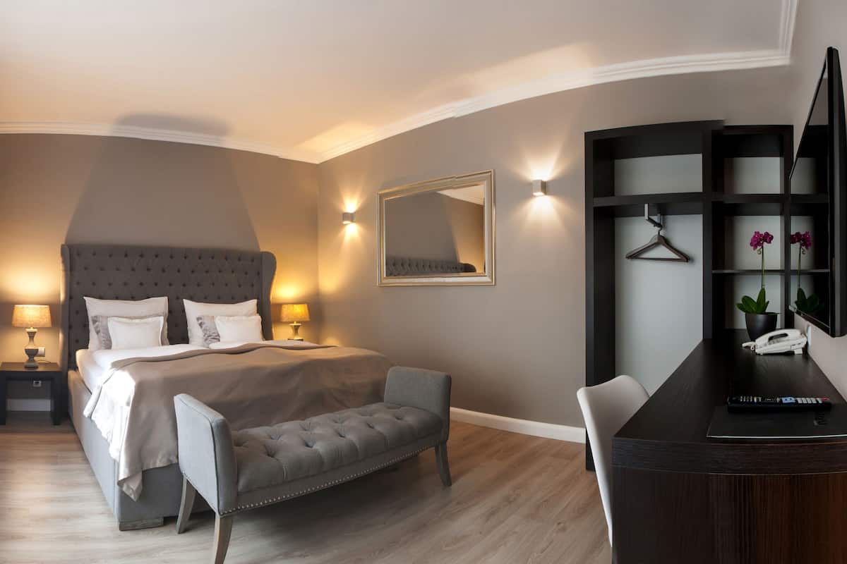 A modern hotel room with a large bed, bedside lamps, a desk with a telephone, and a mirror on the wall.