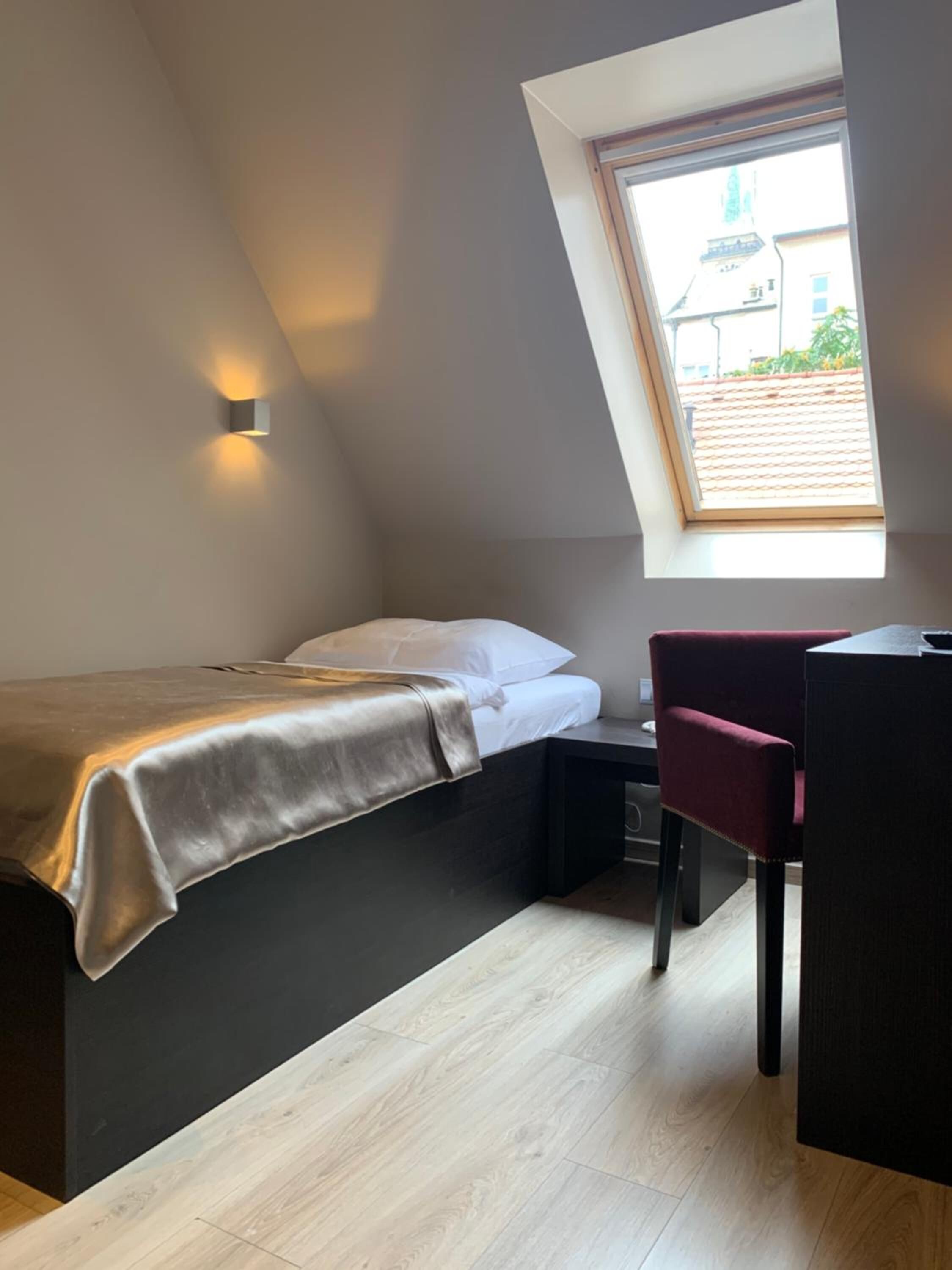 A compact bedroom with a bed, a desk, and a chair. There is a skylight above the bed.