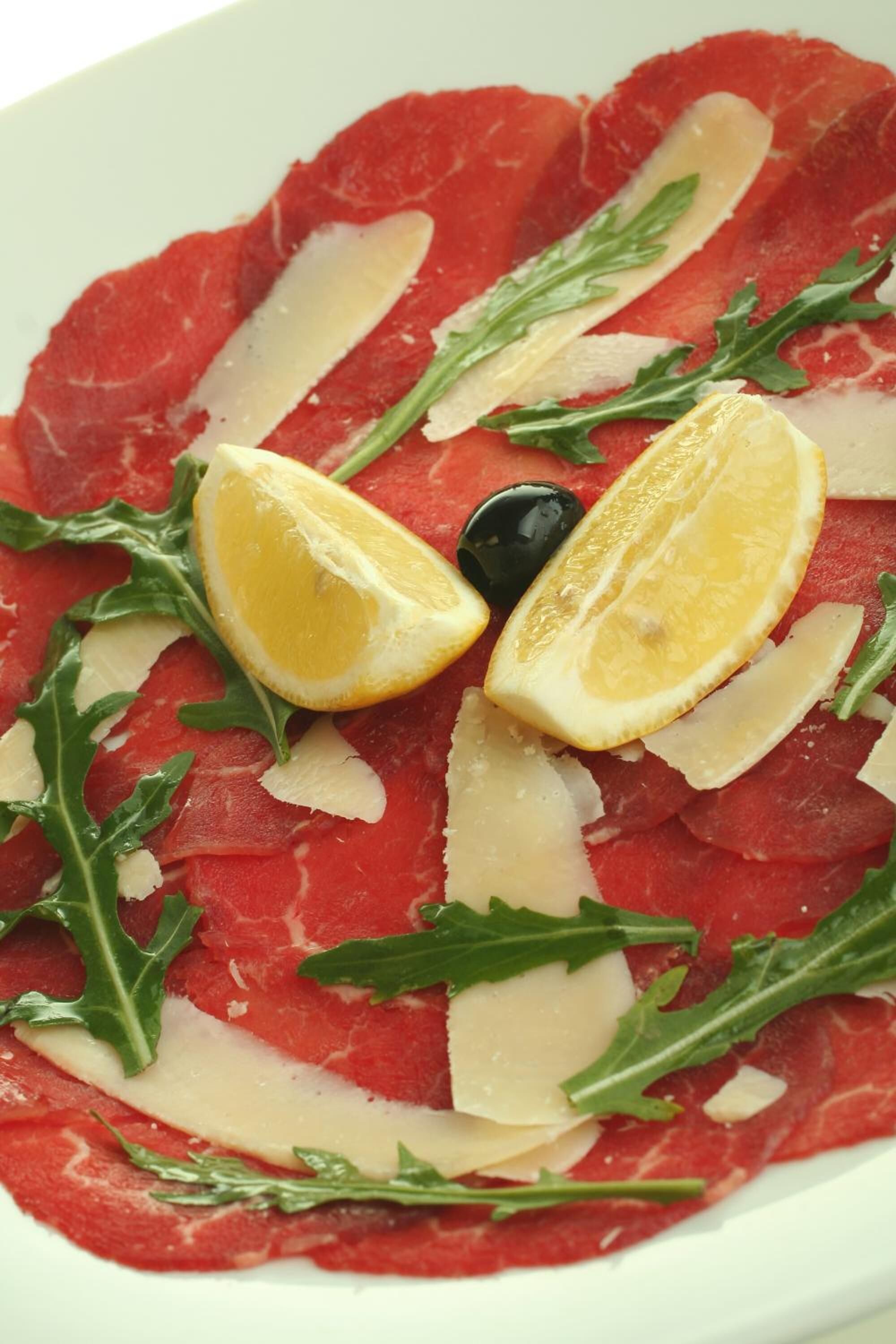 A plate of raw meat with lemon slices, arugula, and black olives.