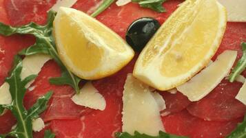 A plate of raw meat with lemon slices, arugula, and black olives.