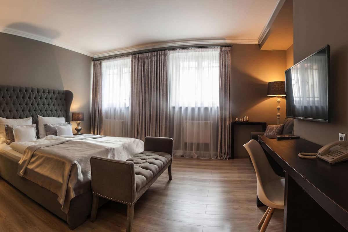 A modern hotel room with a large bed, a desk, a chair, and a TV mounted on the wall.