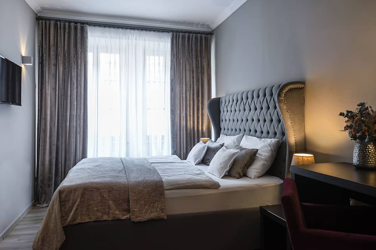 A modern hotel room with a large bed, a flat-screen TV mounted on the wall, and a desk with a vase of flowers.