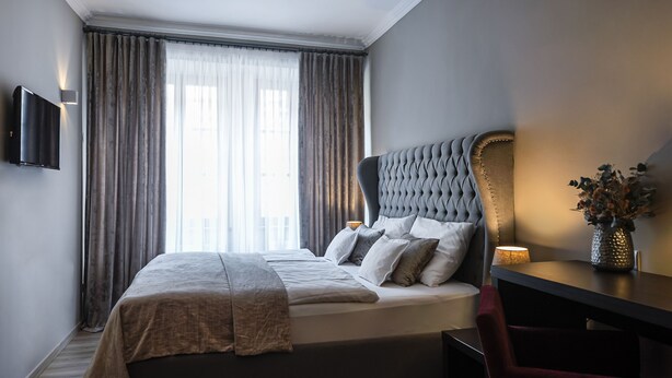 A modern hotel room with a large bed, a flat-screen TV mounted on the wall, and a desk with a vase of flowers.