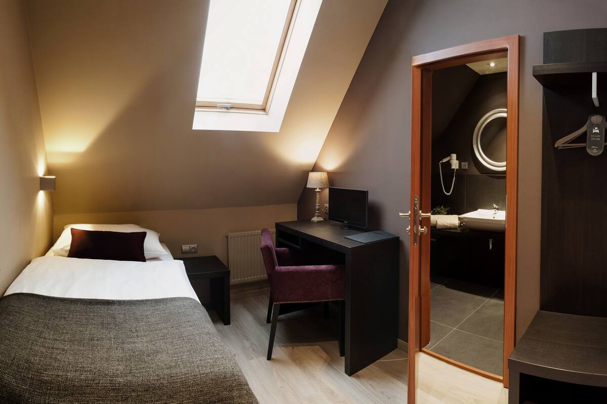 A bedroom with a bed, desk, chair, and a bathroom visible through an open door.