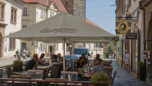 An outdoor café with tables and chairs, a sign for a hotel restaurant, and a building with a tower in the background. - Boutique Hotel Rango (Plzen)