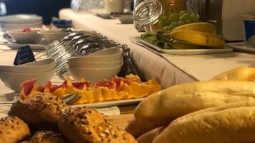 Uma mesa de buffet com diversos alimentos, incluindo pão, frutas e uma cesta de muffins.