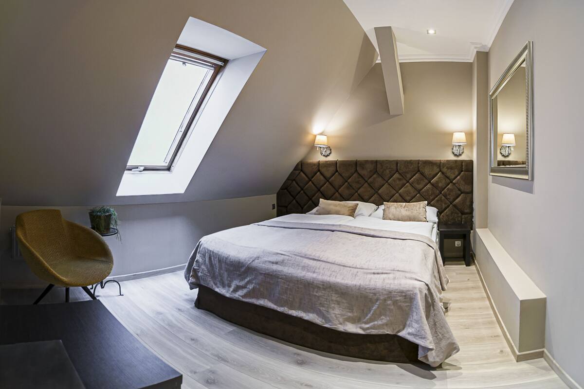 A bedroom with a large bed, a skylight, a chair, and a nightstand.