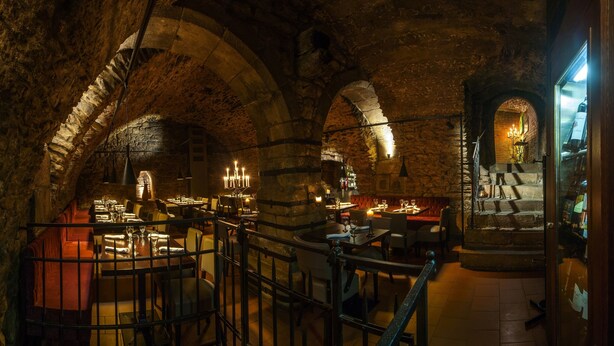 An underground restaurant with stone arches, tables set for dining, and candle-lit chandeliers. - Boutique Hotel Rango (Plzen)