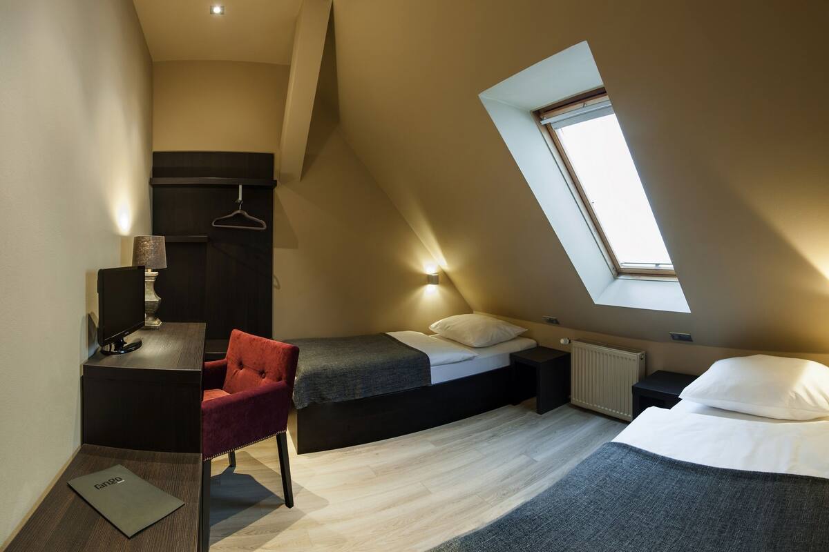 A compact bedroom with a sloped ceiling, a skylight, a desk with a chair, and two beds.