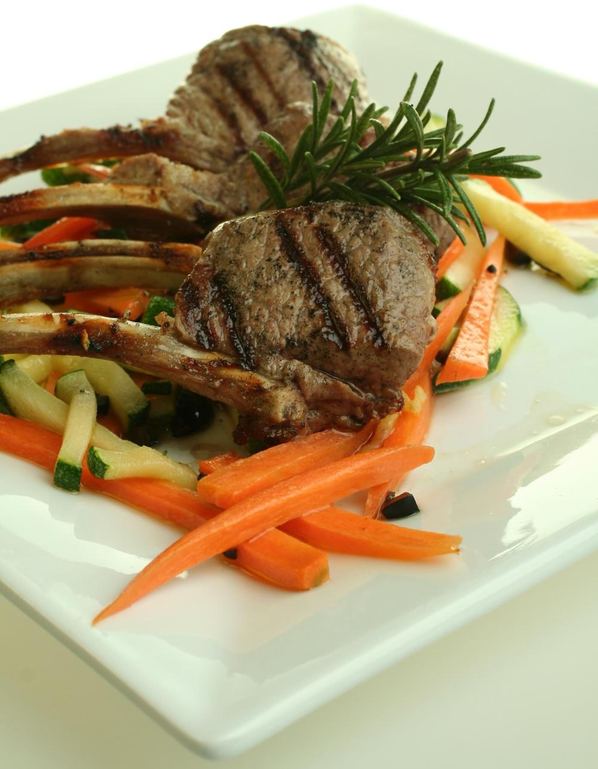 A plate with grilled lamb chops, carrots, and zucchini.