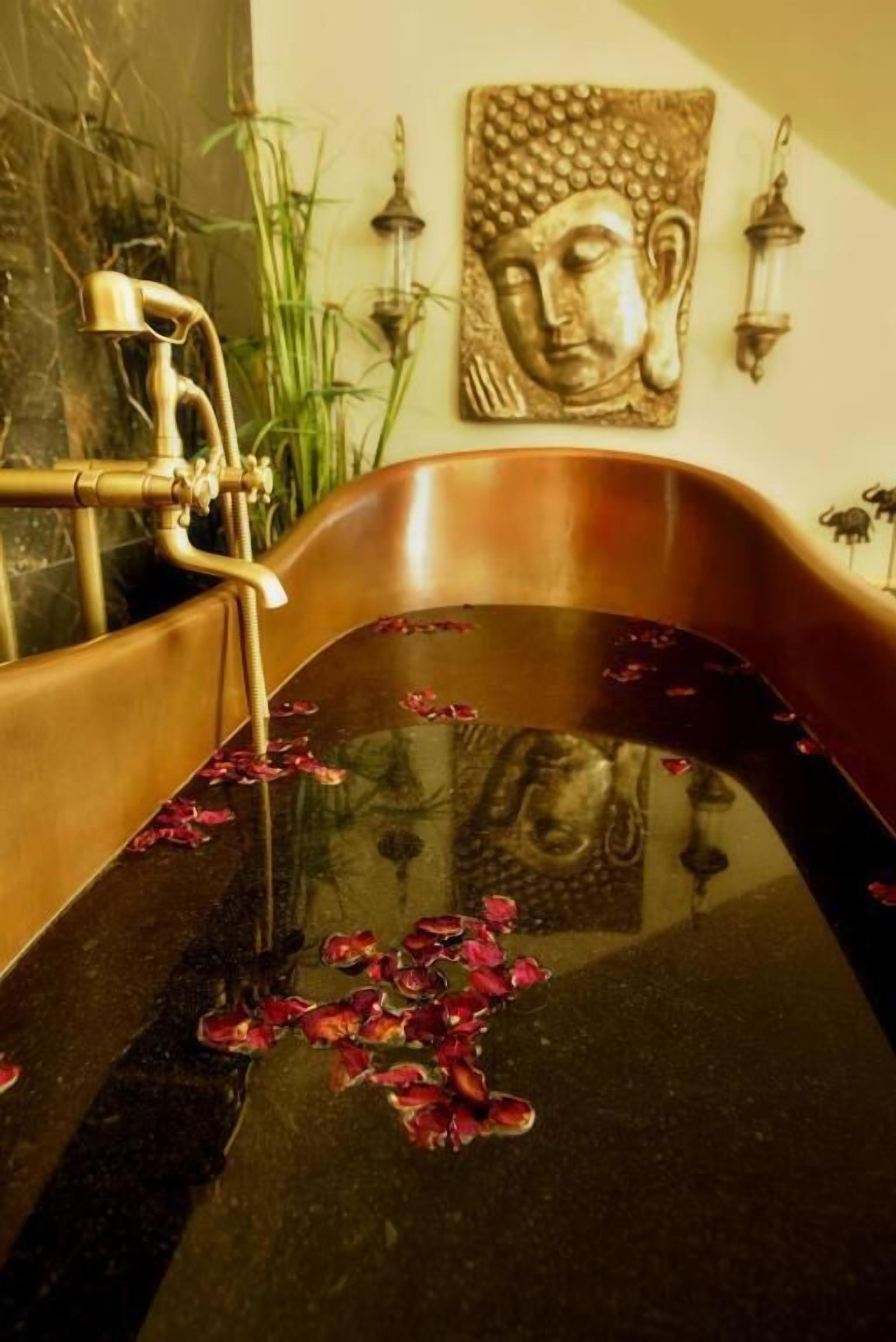 Una vasca da bagno con una statua di Buddha, un bocchello e una scultura di testa di Buddha a parete.