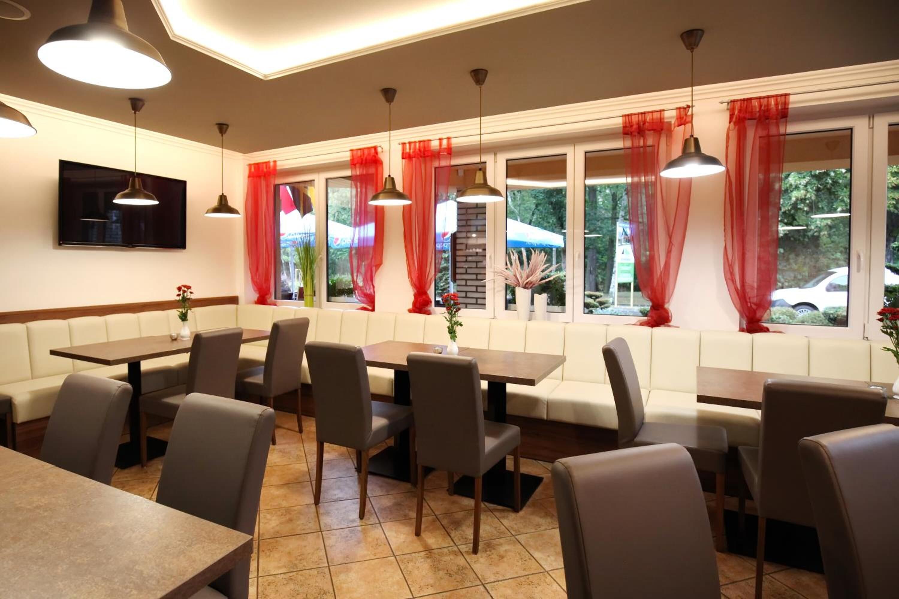Un restaurante con cabinas y mesas, cortinas rojas y luces colgantes.