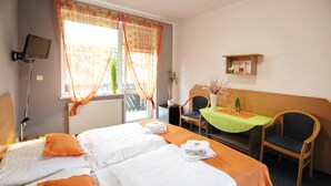 Habitación de hotel con dos camas, un escritorio con silla, un televisor montado en la pared y una ventana con cortinas.