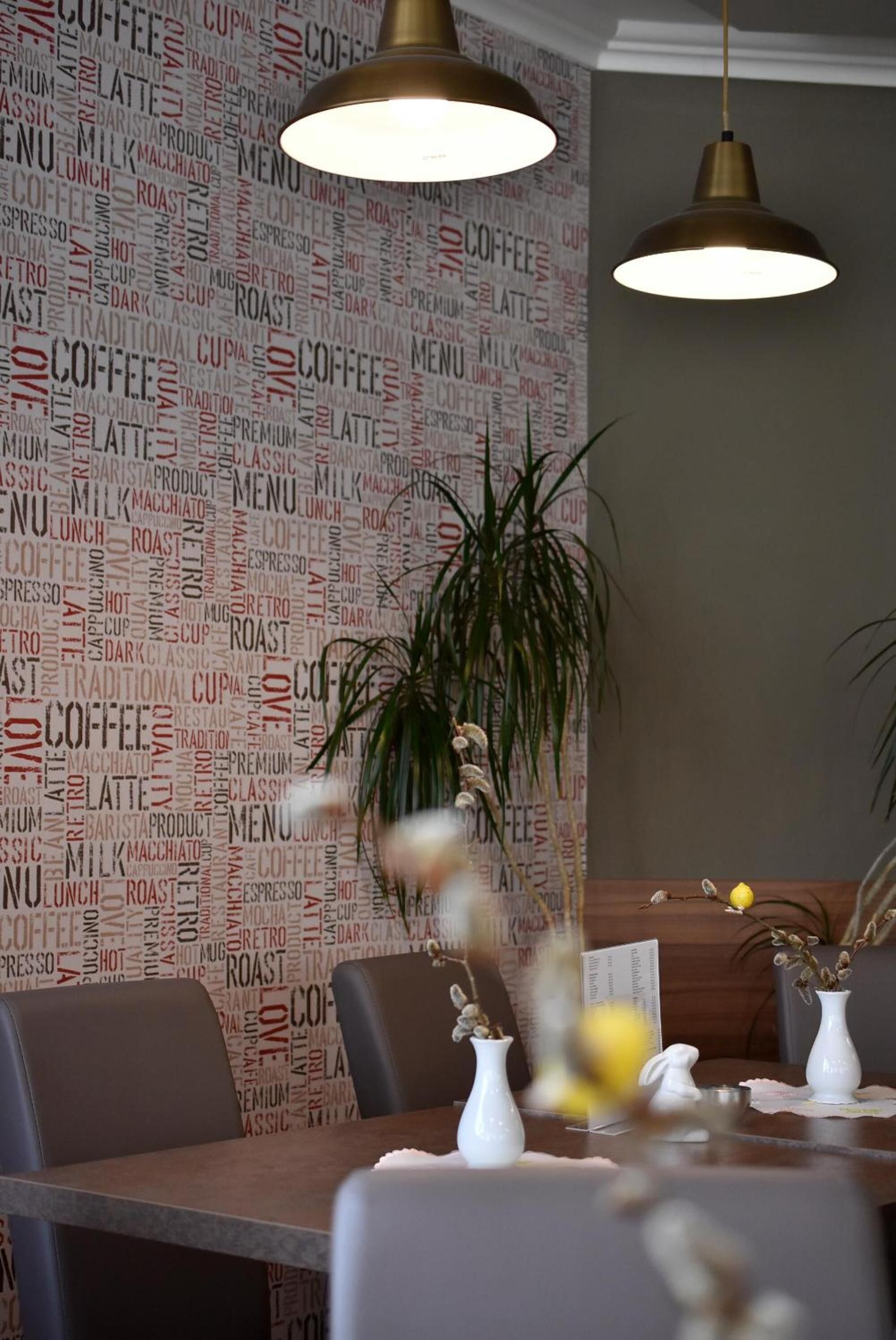 A restaurant interior with a wall covered in coffee-related words, two hanging pendant lights, and a table with white vases and a menu.