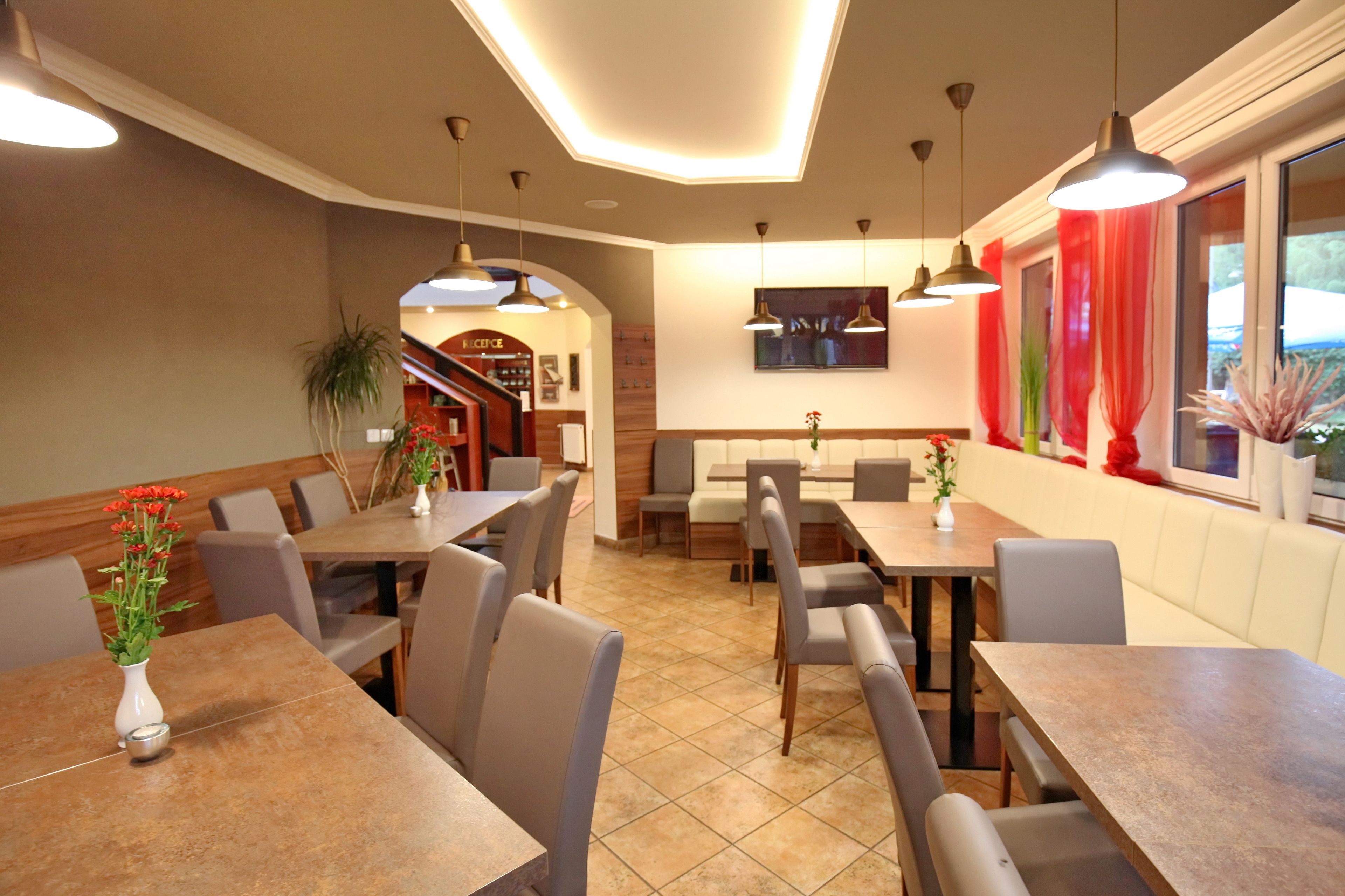 Un interior de restaurante con varias mesas y sillas, una escalera y un amplio ventanal con cortinas.