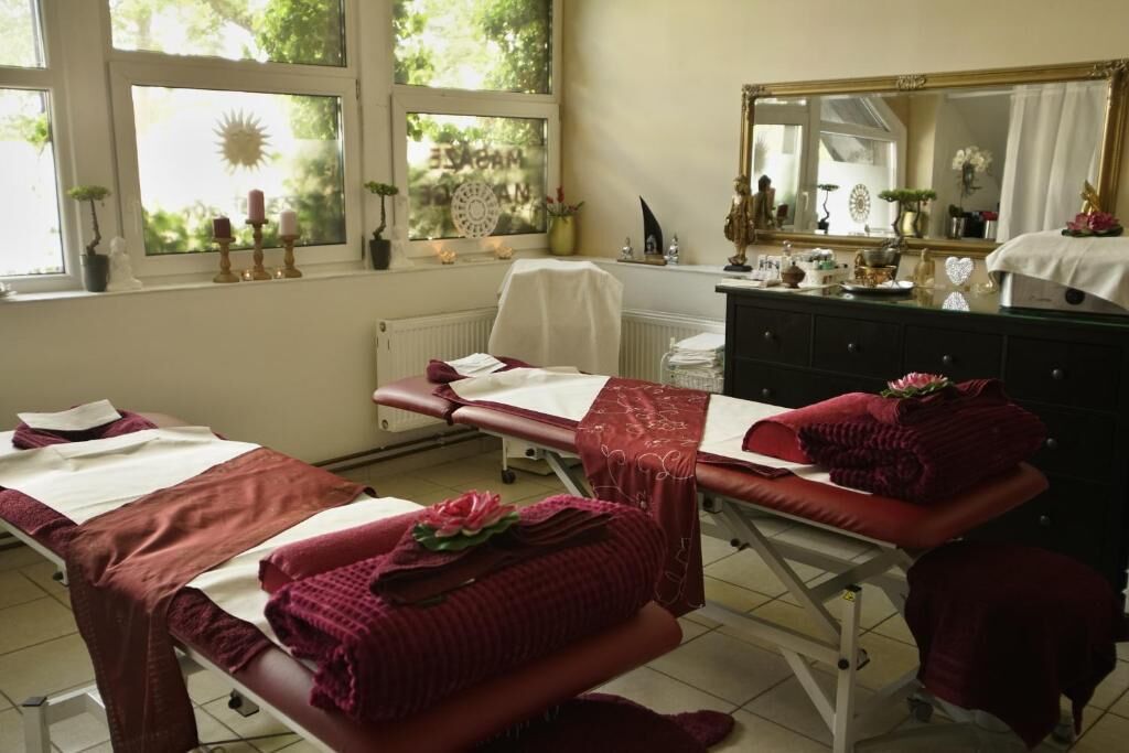 A room with two beds, a window with a view of greenery, a mirror, and a dresser with various items.