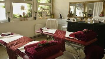 A room with two beds, a window with a view of greenery, a mirror, and a dresser with various items.