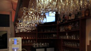 Una zona de bar con numerosos vasos de vino colgando y un televisor al fondo.