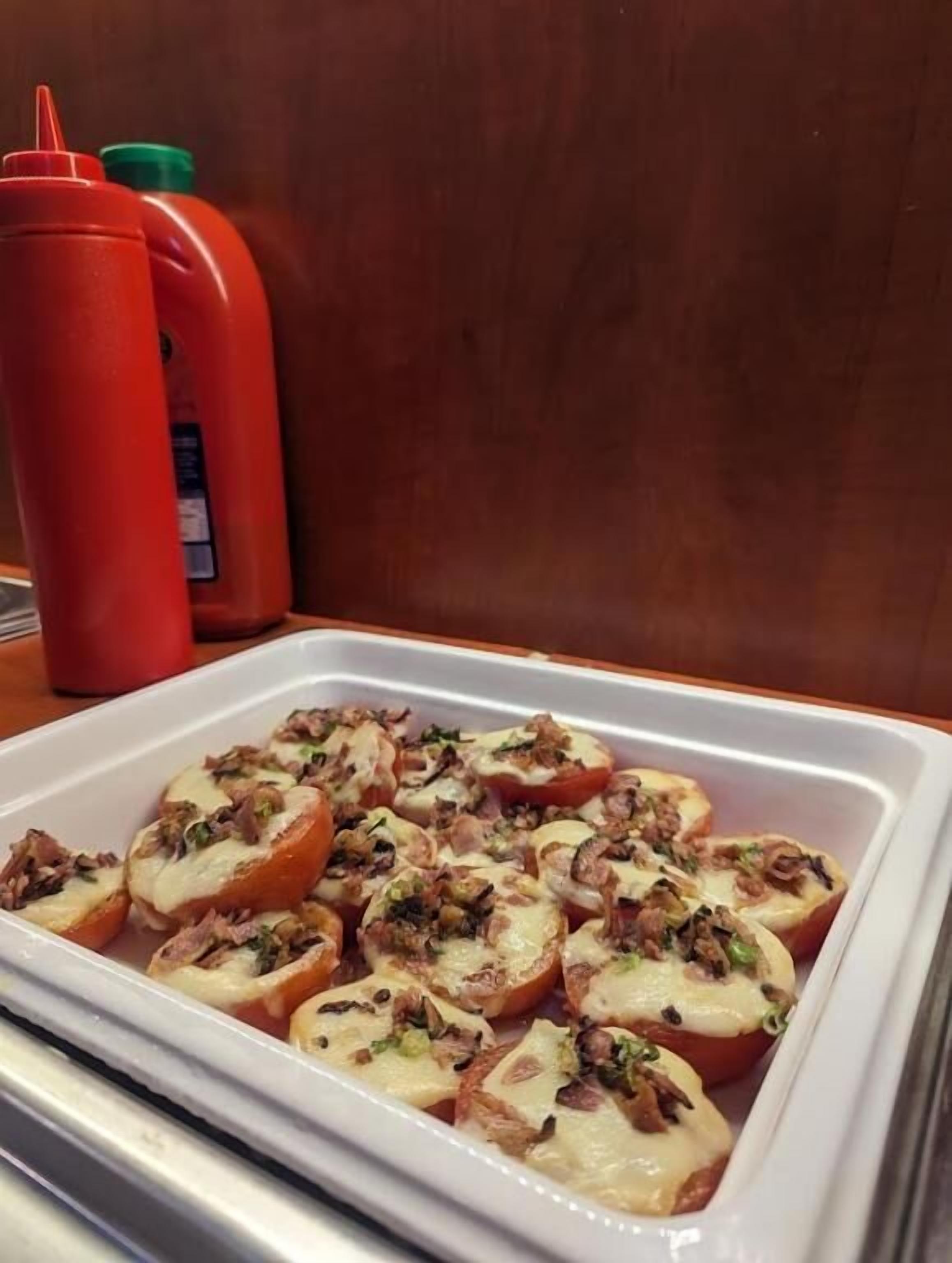 Una bandeja con tomates rellenos de queso y carne, sobre una mesa.