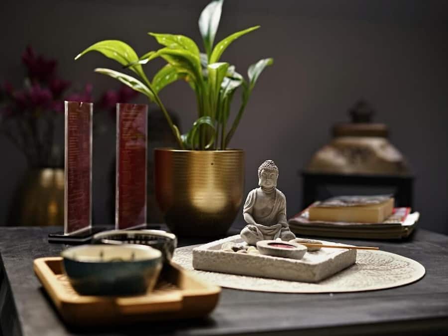 A table with a Buddha statue, incense burner, and a potted plant.