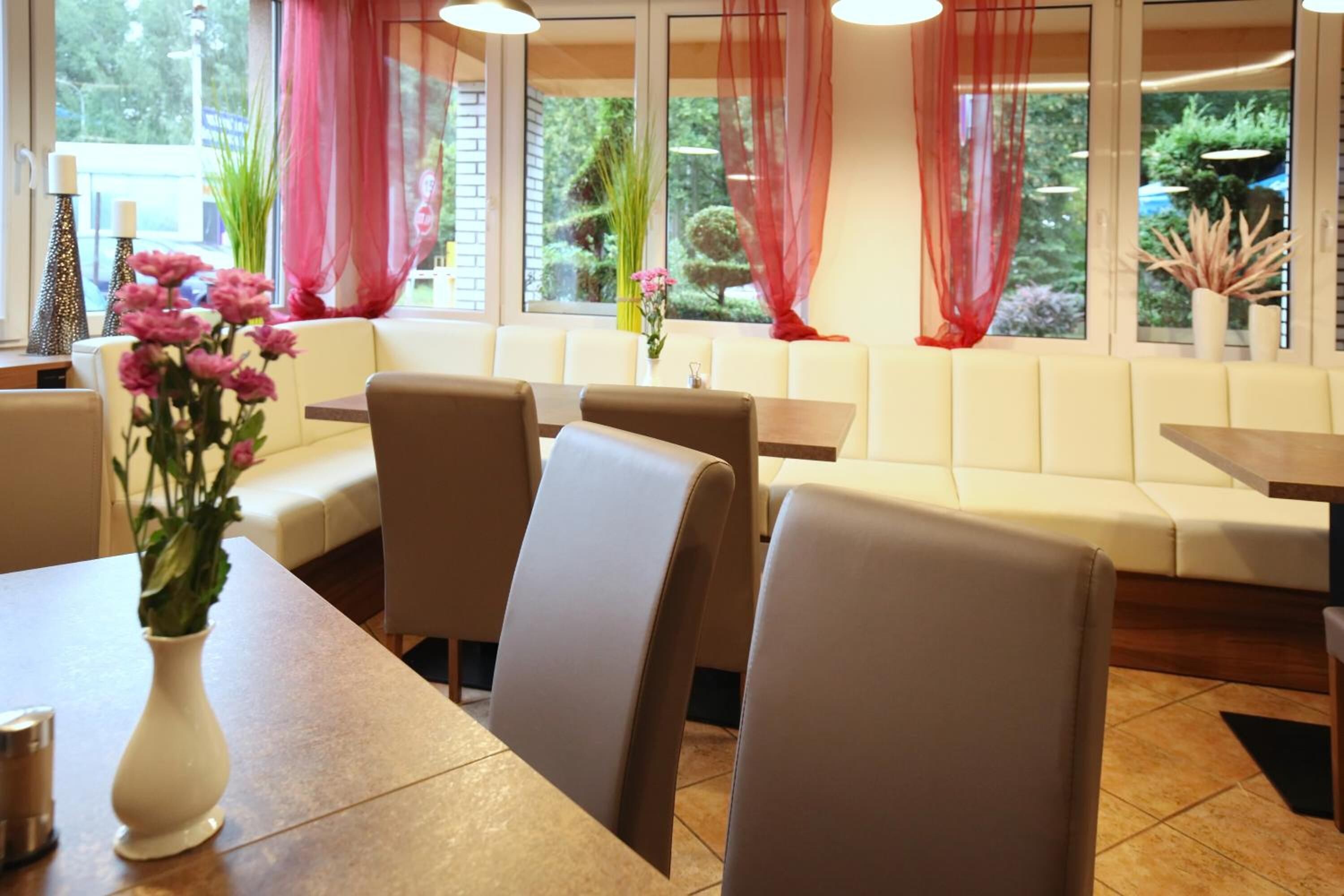 Ein Restaurant mit beigen Stühlen und Tischen, einer weißen Vase mit Blumen und roten Vorhängen.