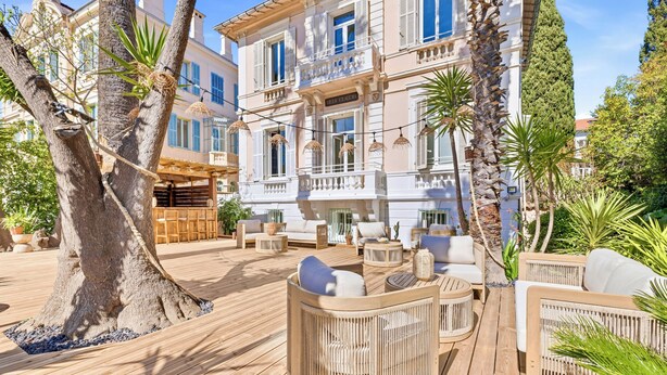 A wooden deck with outdoor seating, a large tree, and a building with balconies. - Villa Claudia Hotel Cannes Centre - Parking (Cannes)