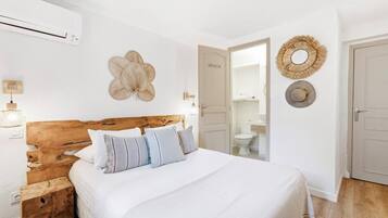 A bedroom with a wooden headboard, a bed with white bedding, a wall-mounted fan, and a door leading to a bathroom.