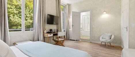 Un dormitorio con cama, escritorio, silla, televisor y puerta que da a un baño.