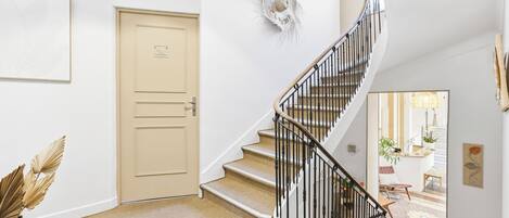A staircase with a beige door, a wall-mounted decorative item, and a view into a room with a plant and a chair.