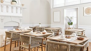 A dining area with wicker chairs and tables, a fireplace, and framed artwork on the walls. - Villa Claudia Hotel Cannes Centre - Parking (Cannes)