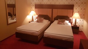Ein Hotelzimmer mit zwei Einzelbetten, jeweils mit einem Nachttisch und einer Lampe. Das Zimmer hat einen roten Teppich und floraler Wandtapete.