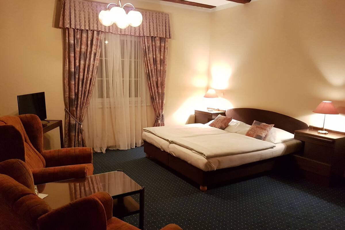 A hotel room with a bed, two bedside tables, a lamp, a chair, a TV, and curtains.