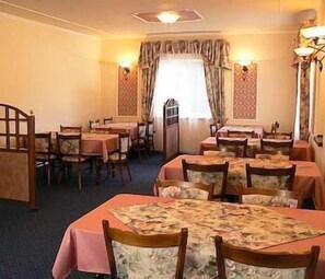 A dining area with multiple tables and chairs, a patterned tablecloth, and a window with curtains. - Eurohotel Garni (Karlovy Vary)