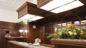 A reception area with a wooden reception desk, a clock, and a telephone. - Hotel Excelsior (Marianske Lazne)