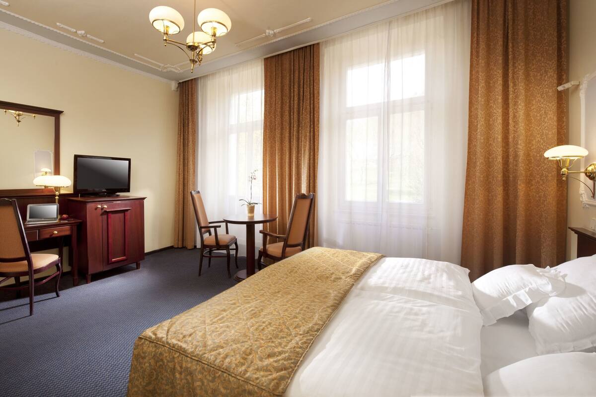 A hotel room with a bed, a desk with a computer, a television, and a chair.