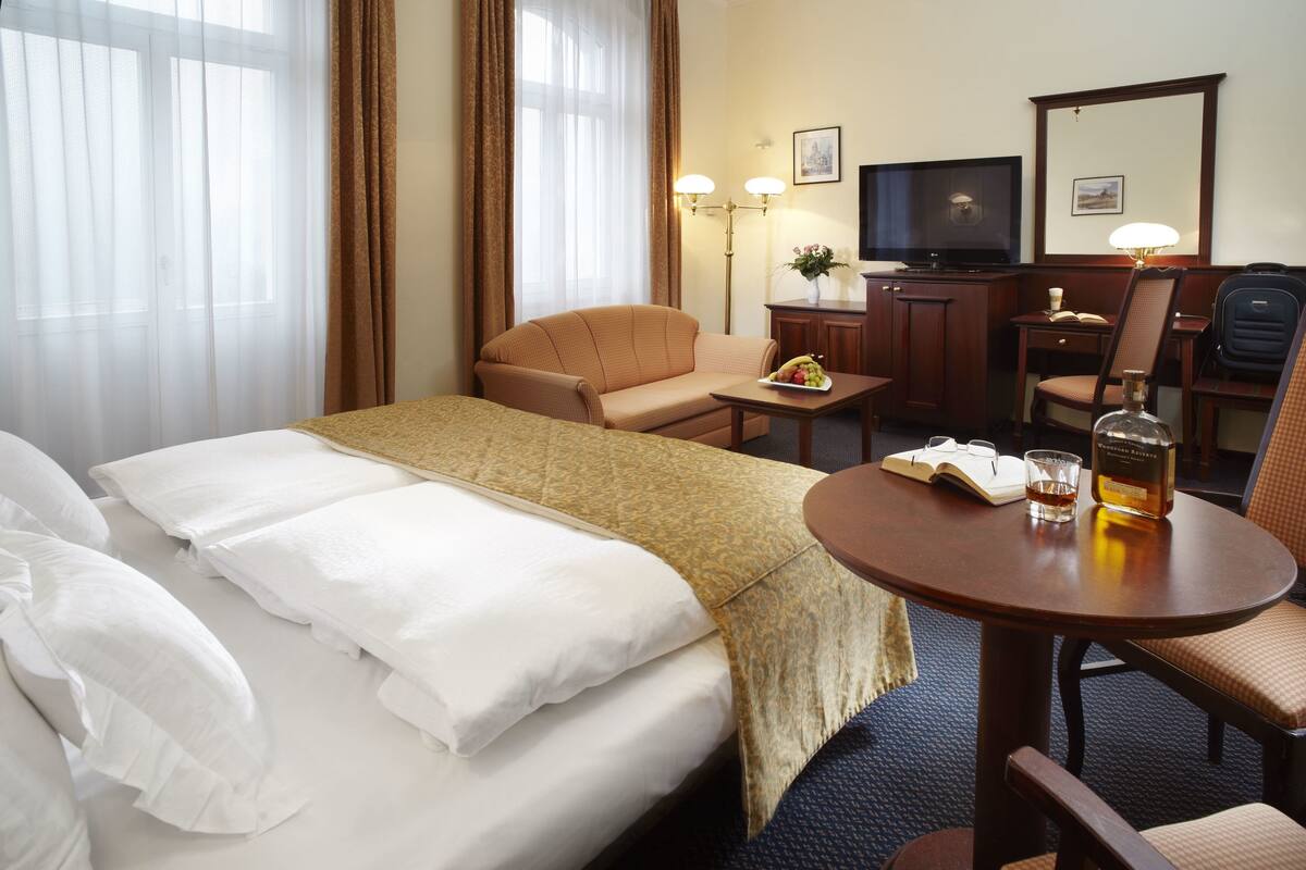 A hotel room with a bed, a desk, a chair, a television, and a lamp.
