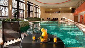 An indoor swimming pool with a table and chairs, a pitcher of orange juice, and a glass of orange juice. - Hotel Excelsior (Marianske Lazne)