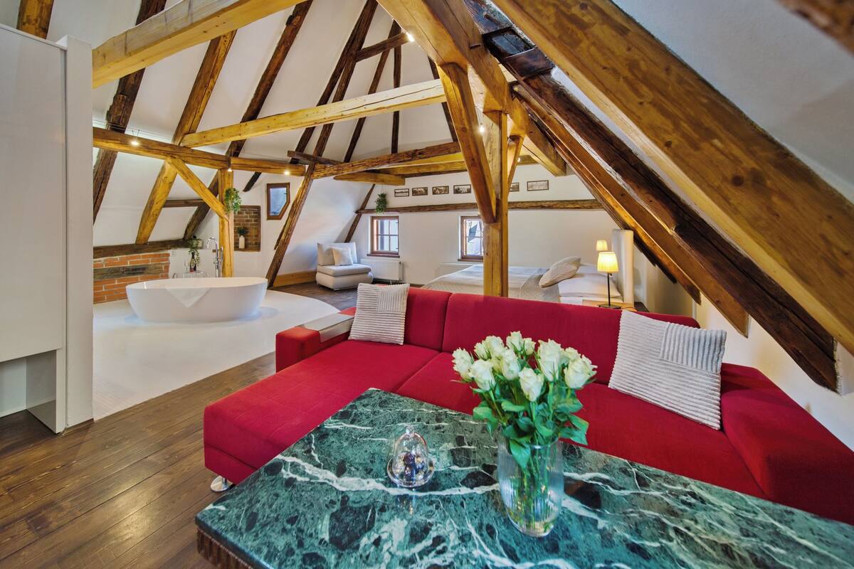 An attic room with a red sofa, a marble coffee table, and a white bathtub.