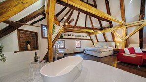 Un amplio dormitorio en el ático con una bañera grande, vigas de madera, un sofá rojo y una pared de ladrillo.