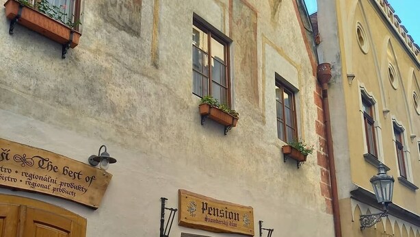 Un edificio con puerta y ventanas de madera, un letrero que dice "Pension" y bancos de madera al aire libre.
