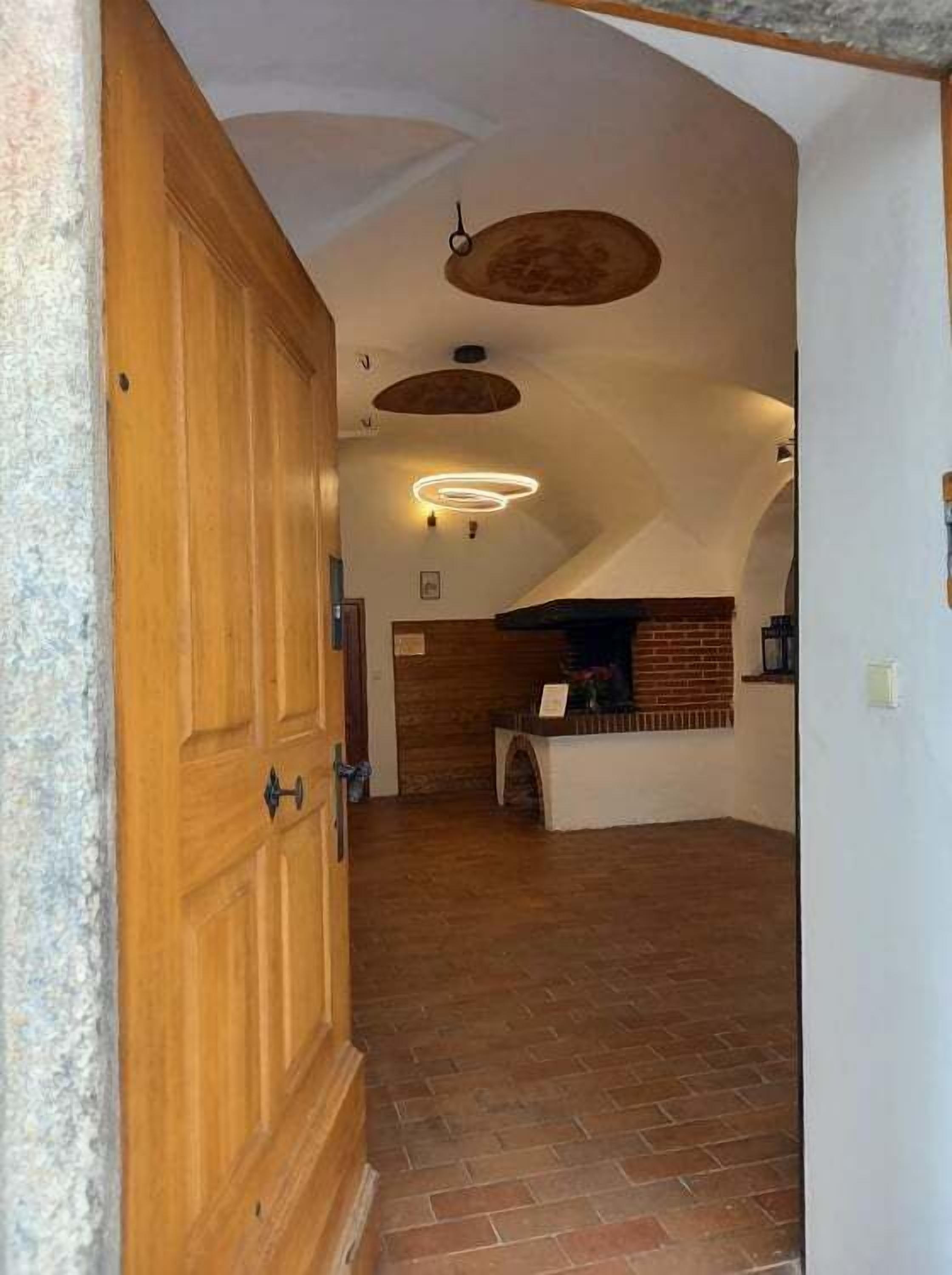 A spacious hallway with a wooden door, a brick fireplace, and a modern light fixture.