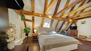 Un dormitorio con techo de madera, una cama, una mesita de noche, una lámpara, una planta en maceta y un televisor.