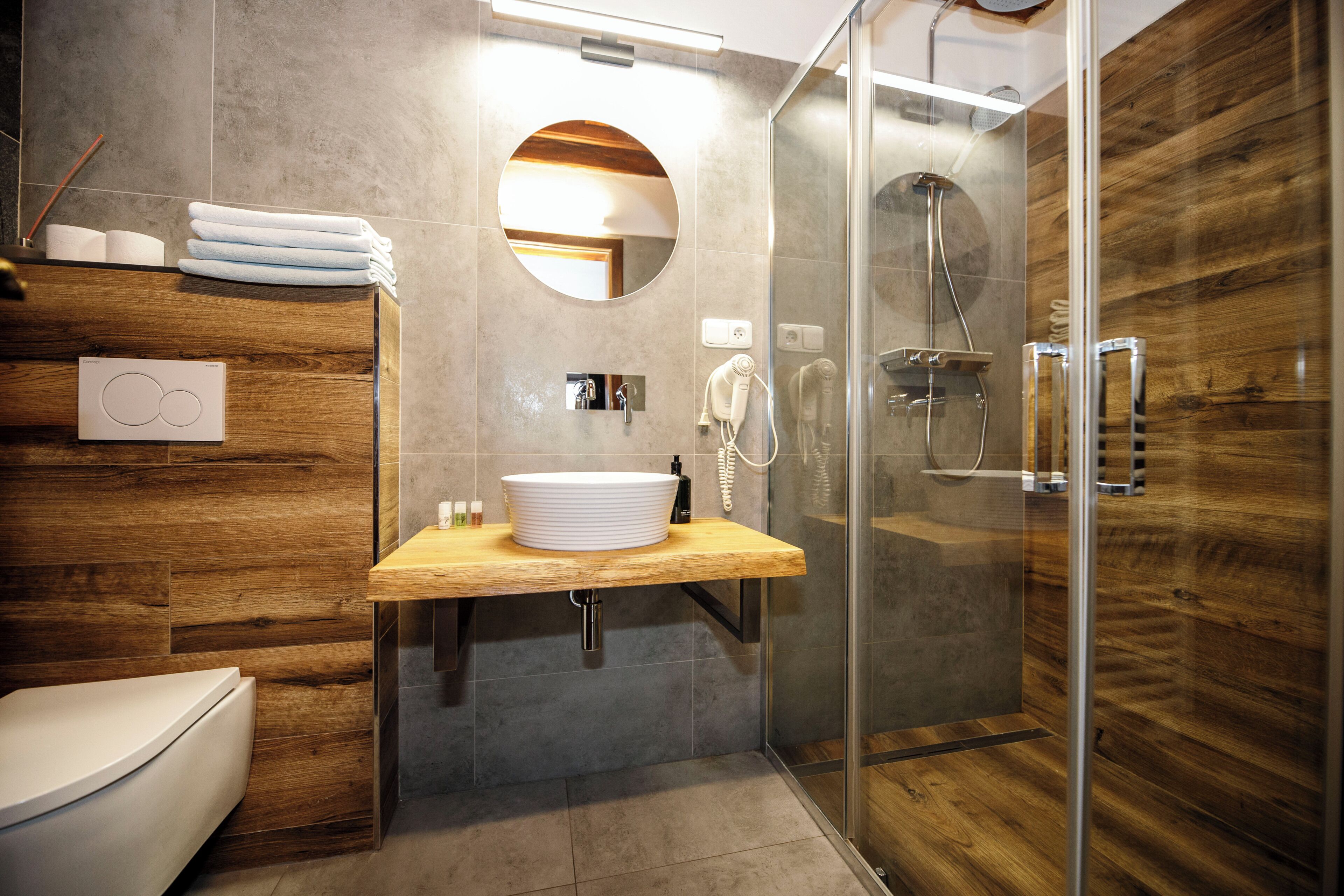 Un baño moderno con tocador de madera, cabina de ducha de vidrio y espejo redondo.