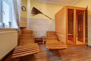 Un sauna con bancos de madera, un reloj en la pared y una escoba apoyada.