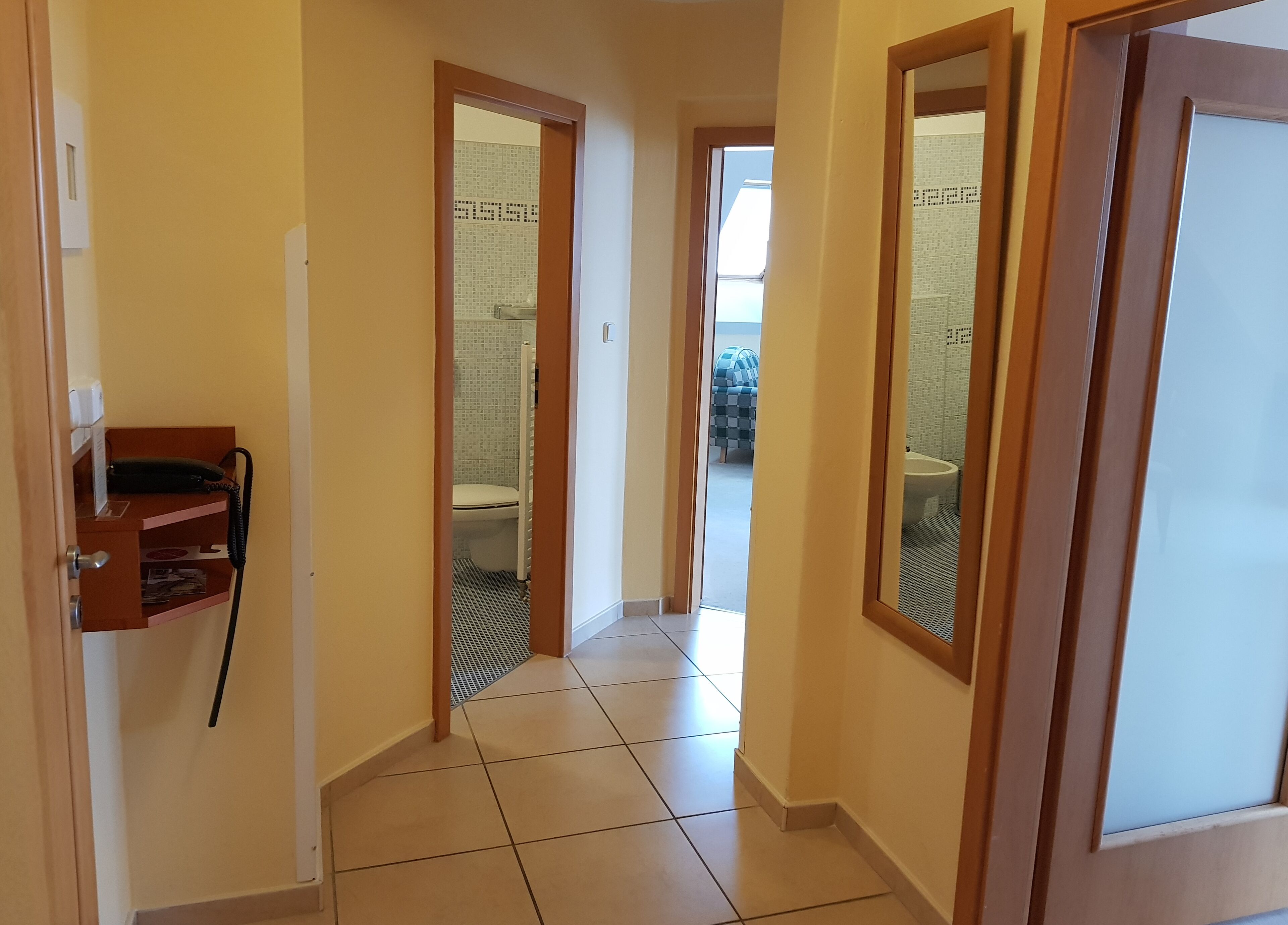 Un couloir avec une porte en bois, un téléphone et un sol carrelé.
