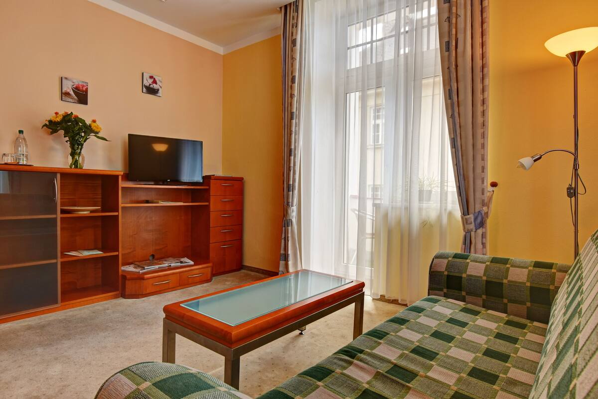 A living room with a sofa, a television, a wooden cabinet, and a glass-top coffee table.