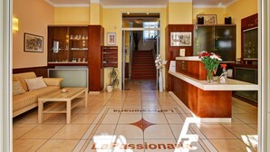 Un vestíbulo de hotel con una recepción, un sofá y una escalera que conduce a los pisos superiores.