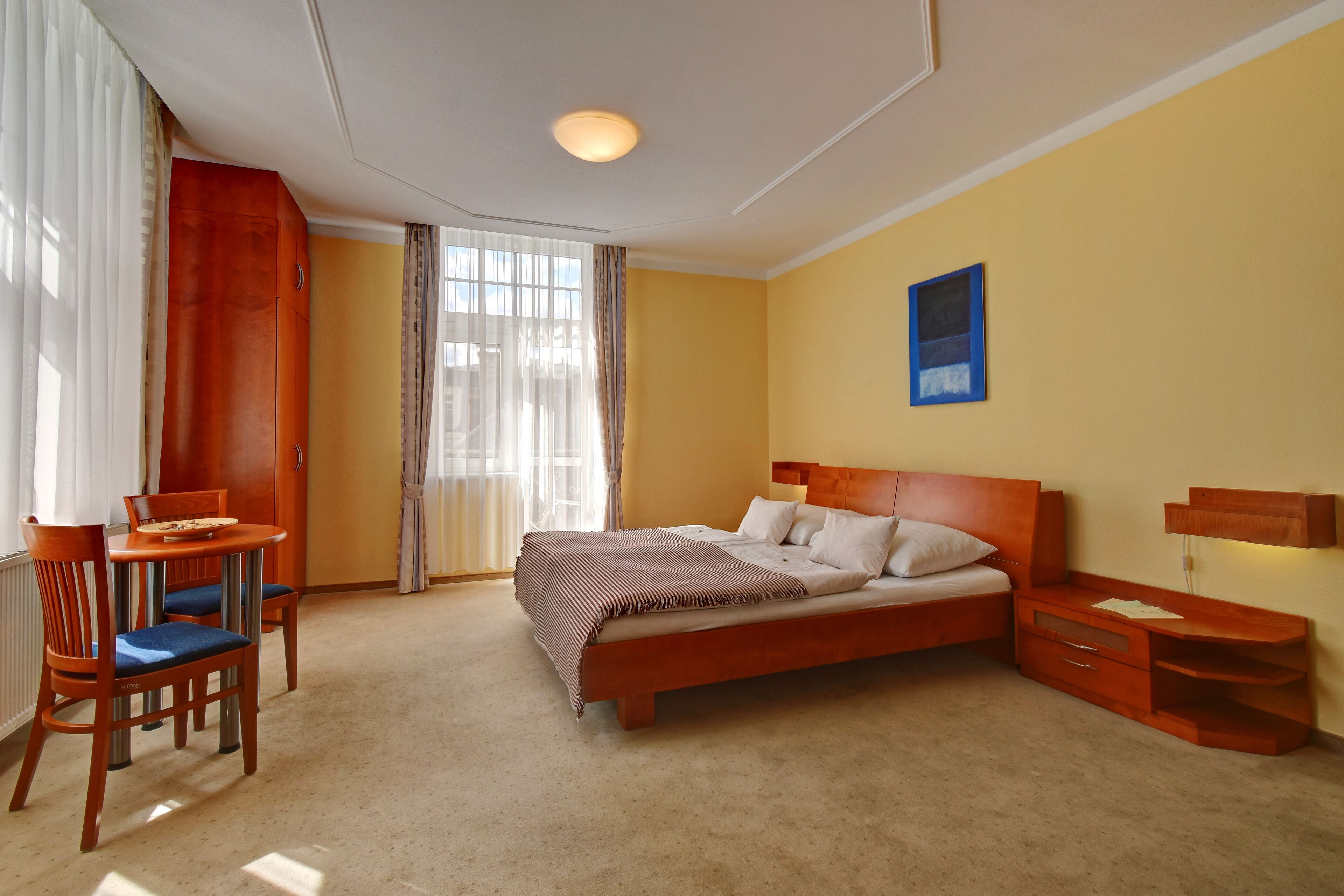 Een hotelkamer met een bed, een bureau met stoel, een klein tafeltje en een nachtkastje.