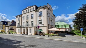 Un hotel de varios pisos con un balcón, un toldo verde y un cartel de estacionamiento.