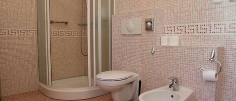 A bathroom with a shower, toilet, bidet, and sink.